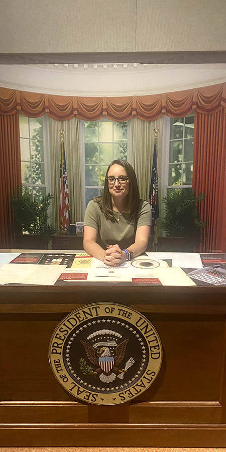 White woman with glasses seated at replica President's desk