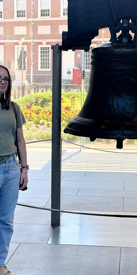 White woman with glasses standing next to the Liberty Bell.