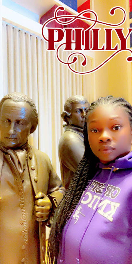 Black woman in a hoodie with a statue of one of the Founding Fathers.