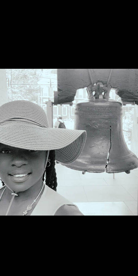 Black woman in a hat standing in front of the Liberty Bell.