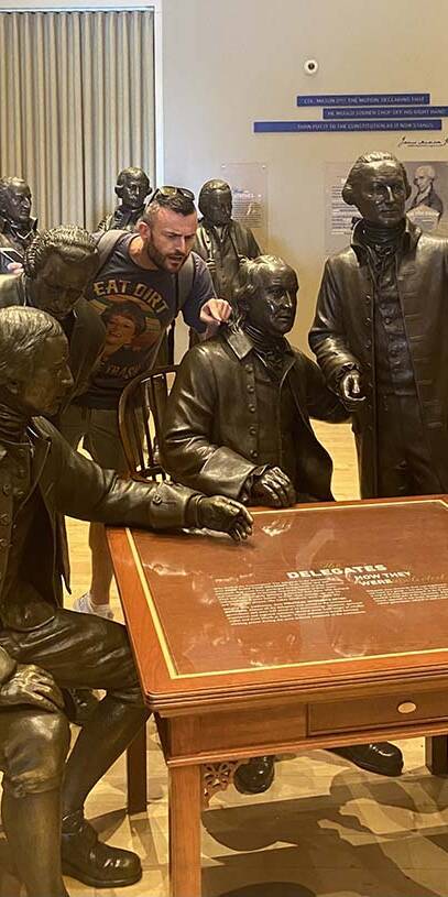 James Sweat posing with bronzae statues of the American Founding Fathers.