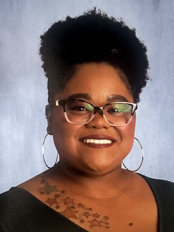 Smiling black woman with glasses, large hoop earrings and natural hair.