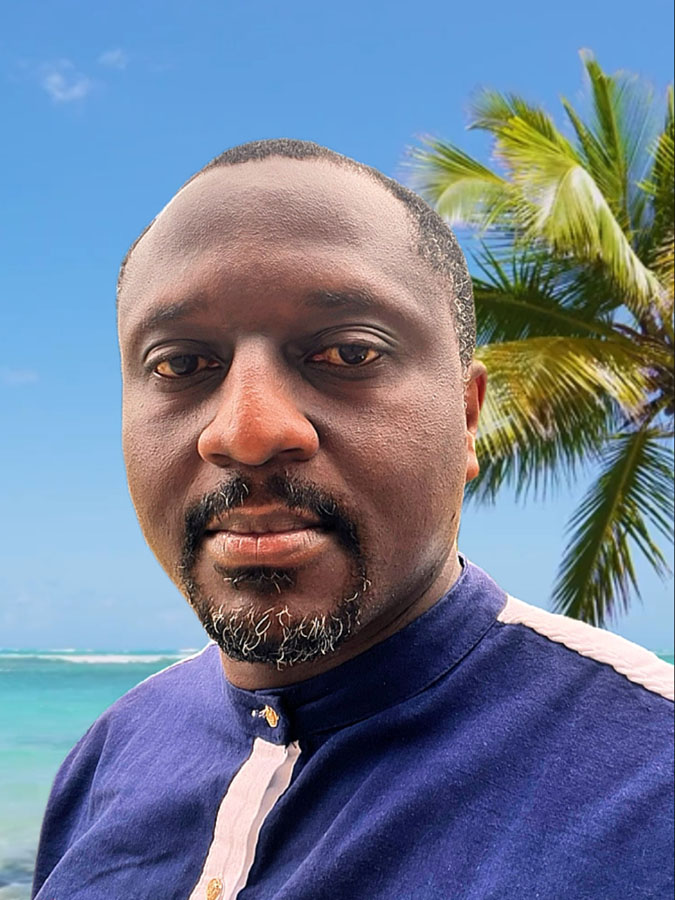 Black man in a collared shirt. A palm tree is visible in the background against a blue sky.