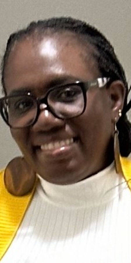 smiling black woman in a white top with a yellow sweater over it.