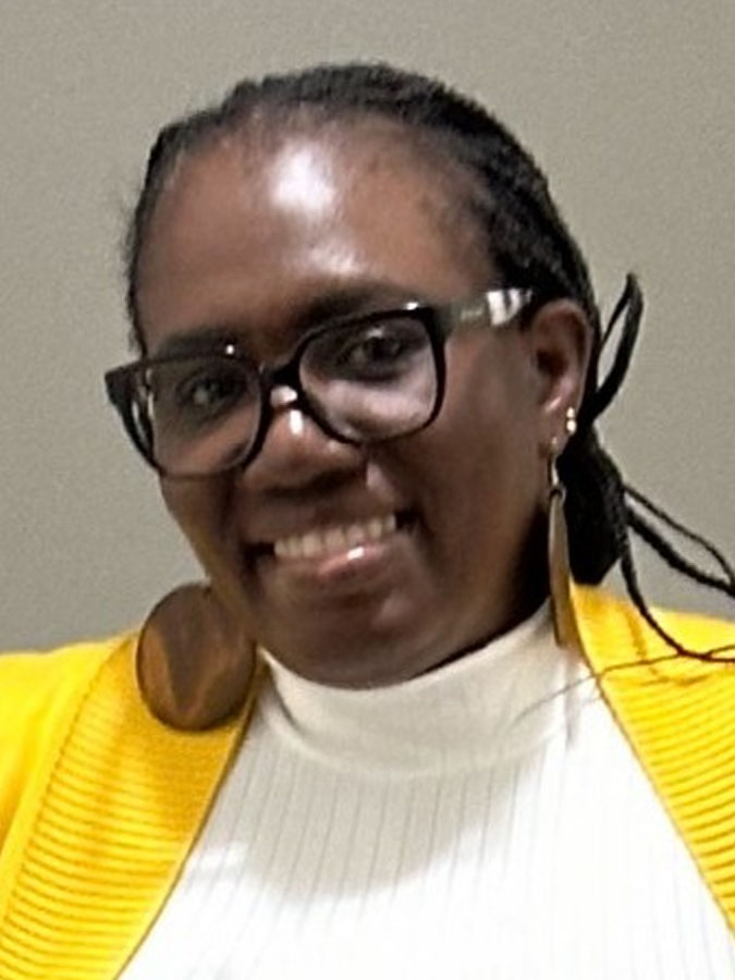 smiling black woman in a white top with a yellow sweater over it.