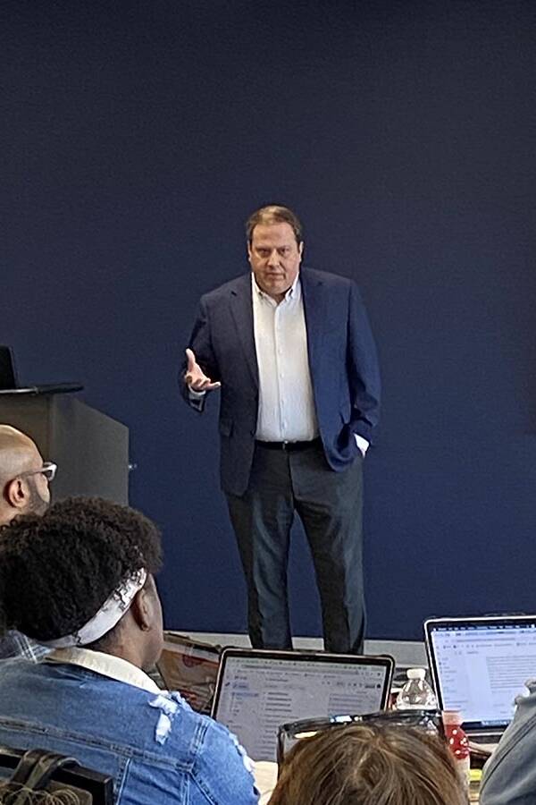 People on laptops watch a man speaking.