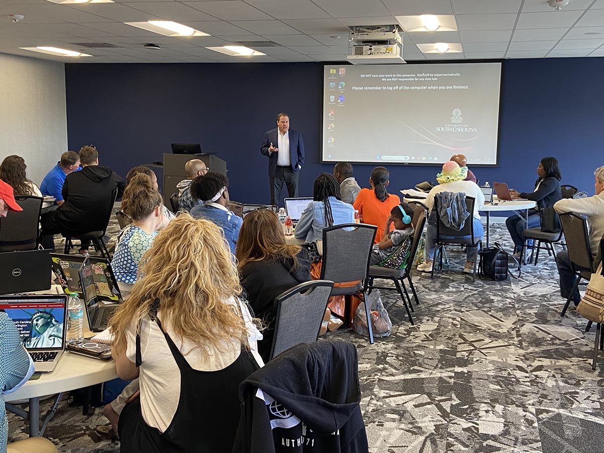 Man in a dark suit jacket speaks to a crowded room.