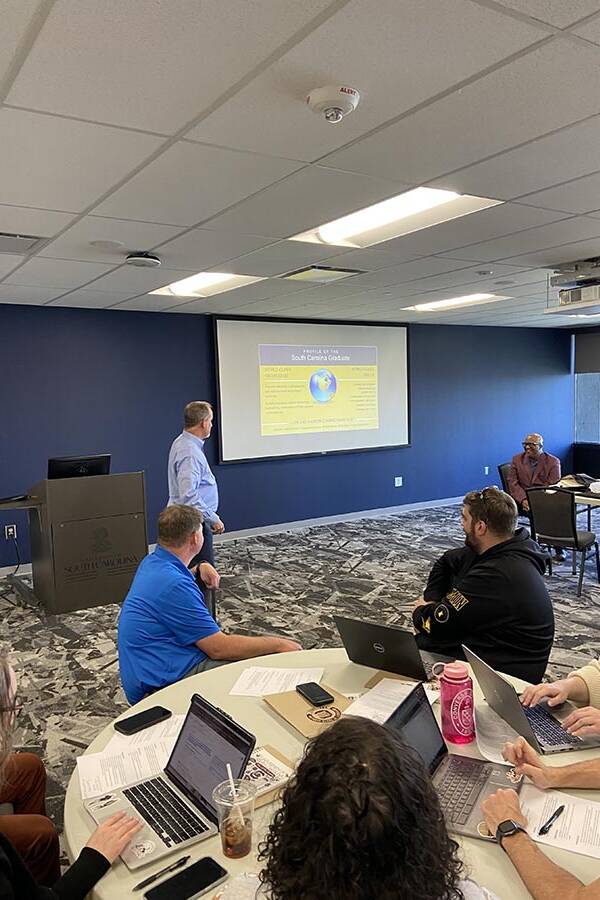 Man in a blue shirt leading a discussion with a slideshow.