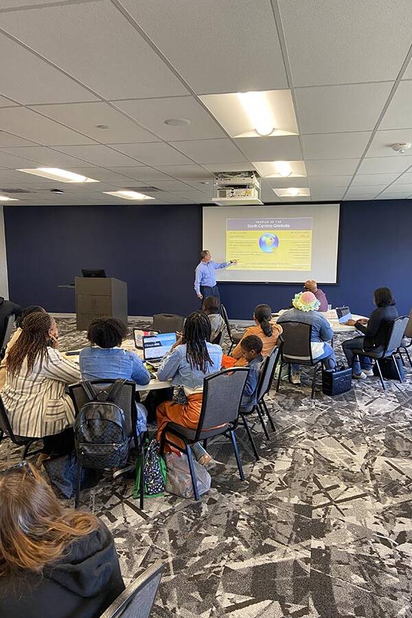 Man in a blue shirt leading a discussion with a slideshow.