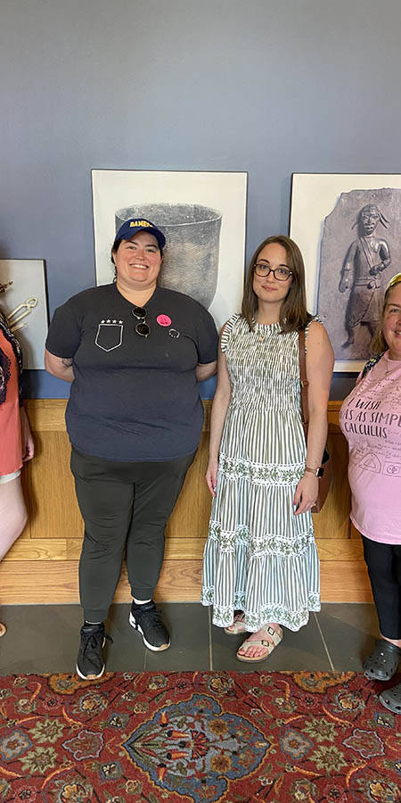 Four women standing in a hallway in front of paintings.