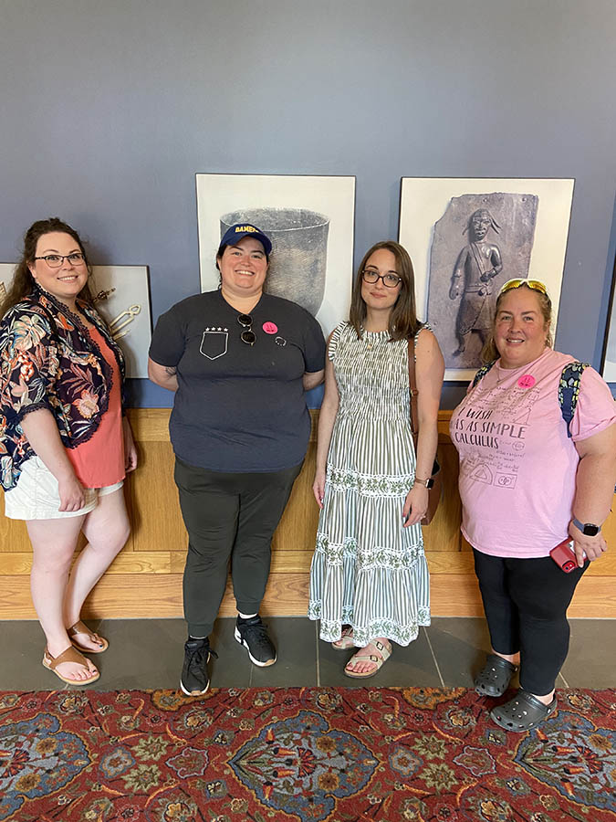 Four women standing in a hallway in front of paintings.
