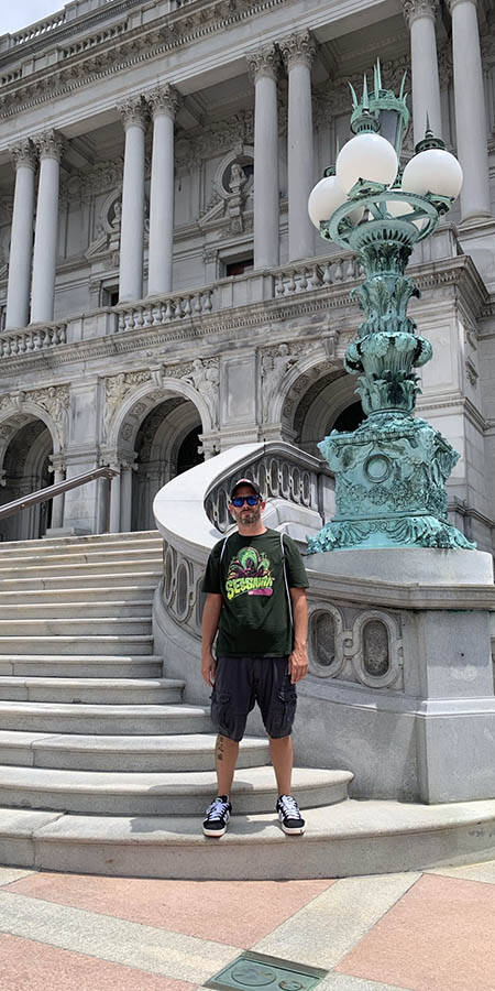 Man in black tshirt and shorts standing on steps of the US Archives Building in Washington DC