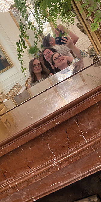a photo of three women smiling at a mirror.