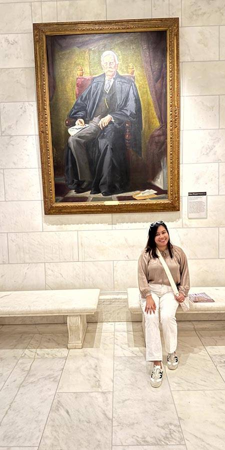 Woman sitting under a painting of a stern-looking man.