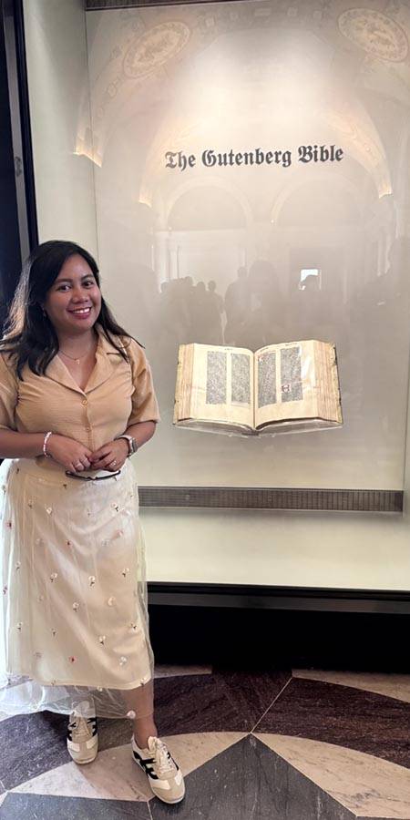 Smiling woman at museum display of The Gutenberg Bible.